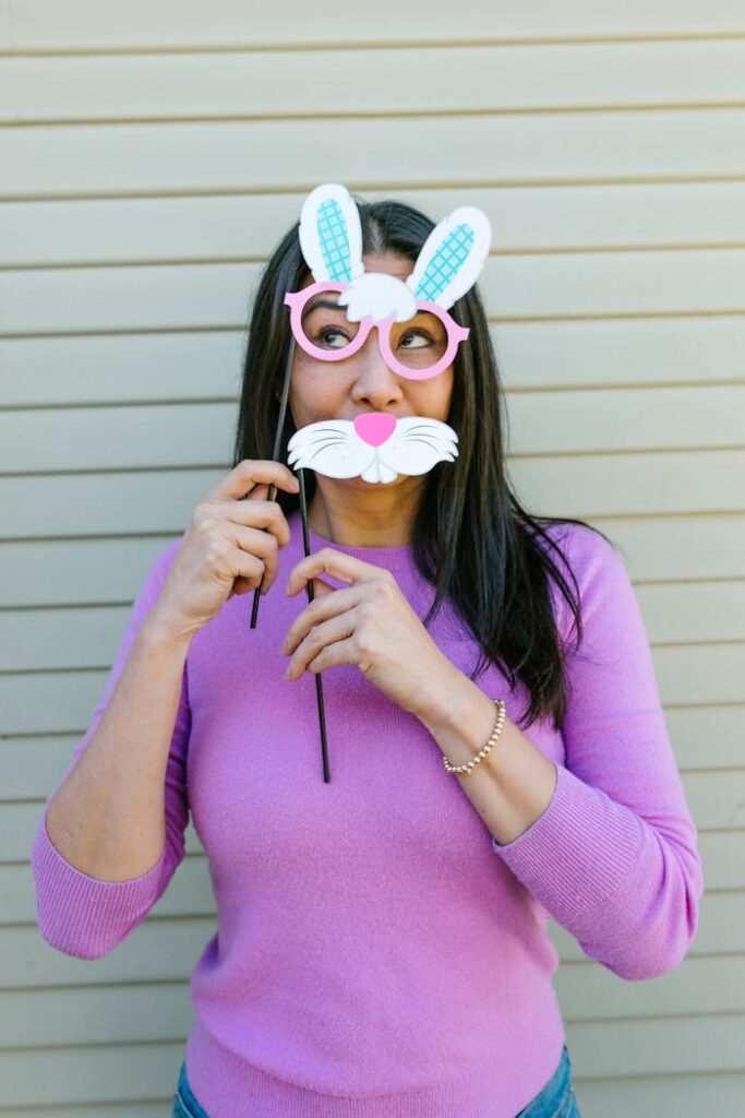 Woman wearing a pink sweater holding an Easter bunny mask against a beige background.